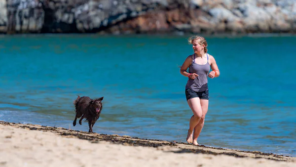 dog running with woman on beach